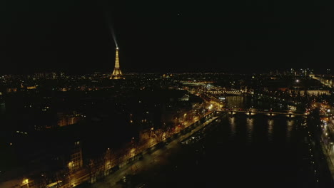 Vista-Panorámica-Aérea-De-La-Ciudad-Nocturna.-Volar-Hacia-Atrás-Sobre-El-Río-Sena,-La-Famosa-Torre-Eiffel-En-La-Distancia.-París,-Francia