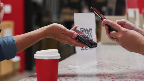 Midsection-of-caucasian-woman-making-contactless-phone-payment-over-cafe-counter