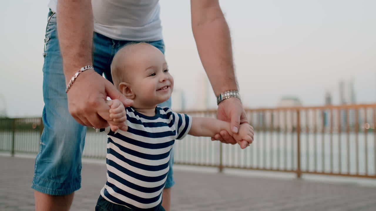feliz y lindo bebé aprende a caminar y da sus primeros pasos en la ciudad bajo el control de su abuelo