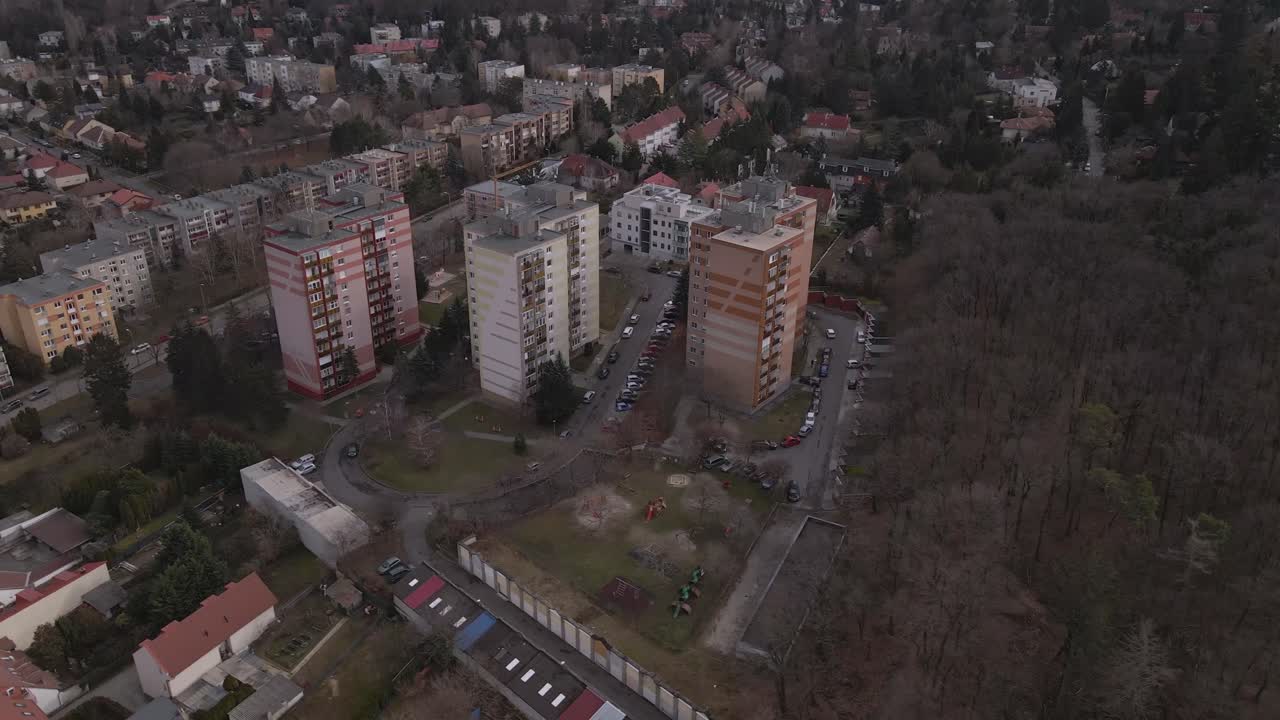 An aerial view of three residential apartment buildings surrounded by greenery and a nearby forest.