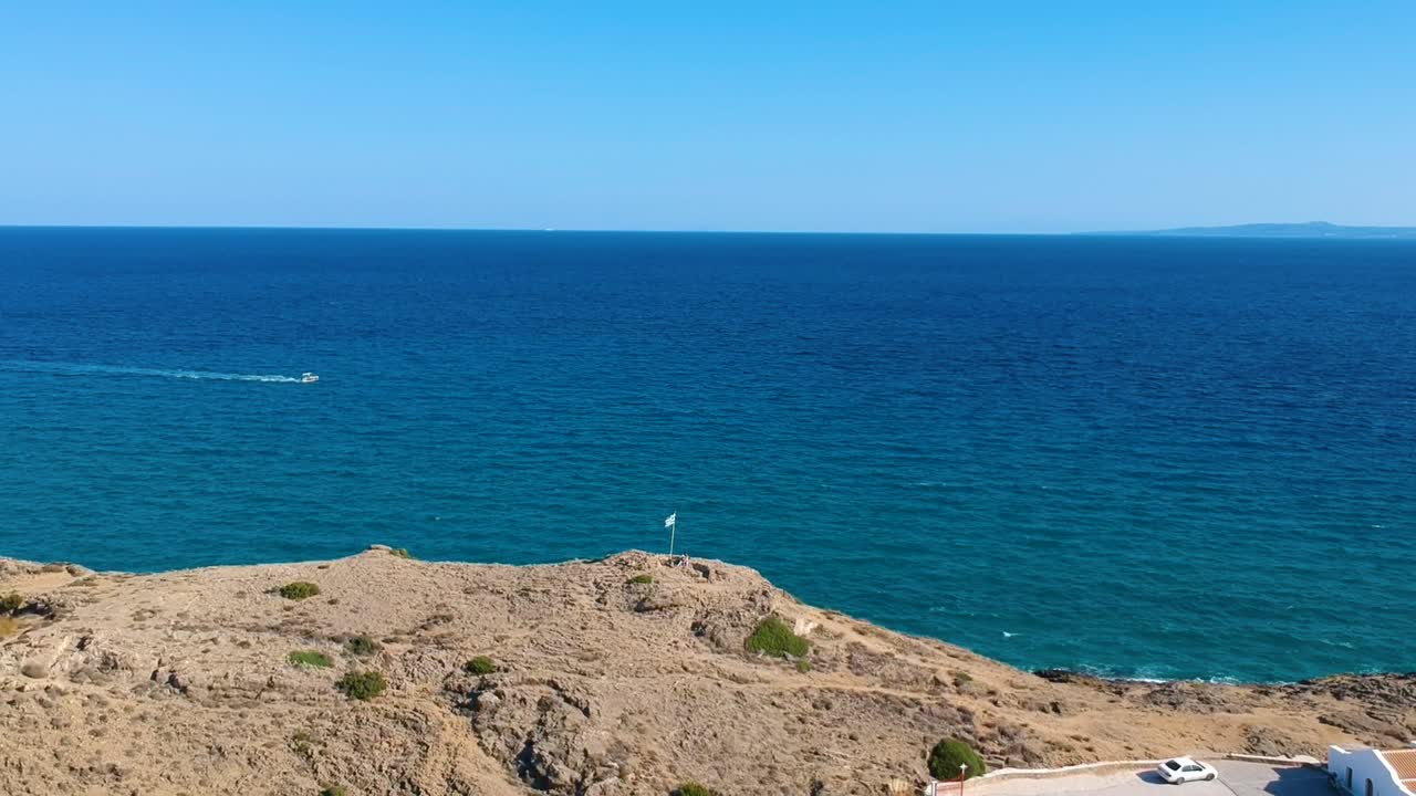 Greek flag on top of Point St. Nicholas at the far east of the Zakynthos Island in Greece with church right, Aerial drone dolly-out reveal shot