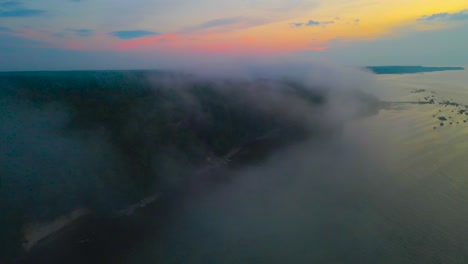 stunningly beautiful aerial drone footage gliding through mist and fog during a sunset or sunrise night dusk dawn time over a rovky beach shoreline in a beach with a tall limestone cliff visible also
