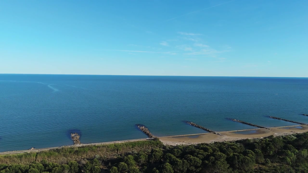 イタリアのエラクレアとピアヴェ川河口付近で、緑のラグーン湿地帯と穏やかな海の波を隔てる長い砂嘴を追跡する、夕暮れ時の高広角ドローンパノラマ。