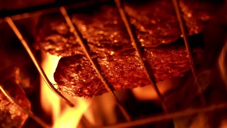 Fat-dripping-from-hamburgers-on-the-grill,-over-the-fire,-with-dark-background