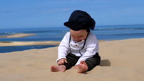 Close-up-shot-of-cute-baby-playing-with-sand-on-Dune-Du-Pilat-with-ocean-in-background---France,Europe