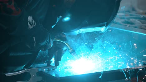 worker in welder's helmet is welding aluminium metal