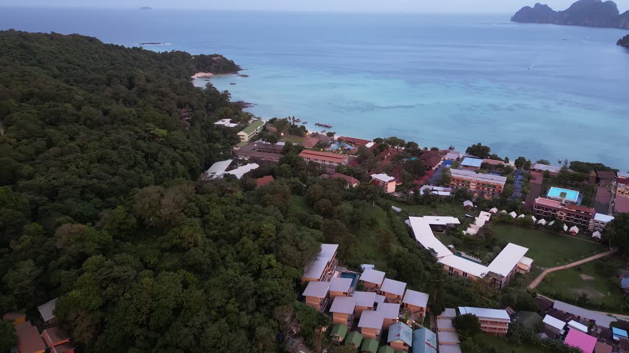 A breathtaking sunset dolly shot over Koh Phi Phi, Thailand, slowly panning down to reveal a luxurious resort nestled among the forest.
