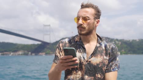 young thoughtful man texting by phone by the sea.
