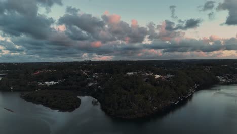aerial of georges river near oatley with forested shores, still waters and moody sky at dusk, establishing overview