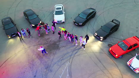 dance group performing near the race cars. young people take turns to dance in the middle. top view. karting at backdrop.
