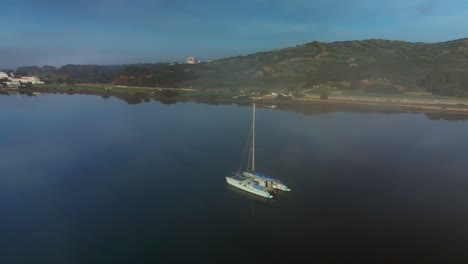 Catamarán-De-Lujo-Flotando-Frente-A-La-Costa-De-Menorca,-España-Con-Aguas-Cristalinas-Que-Rodean-El-Velero