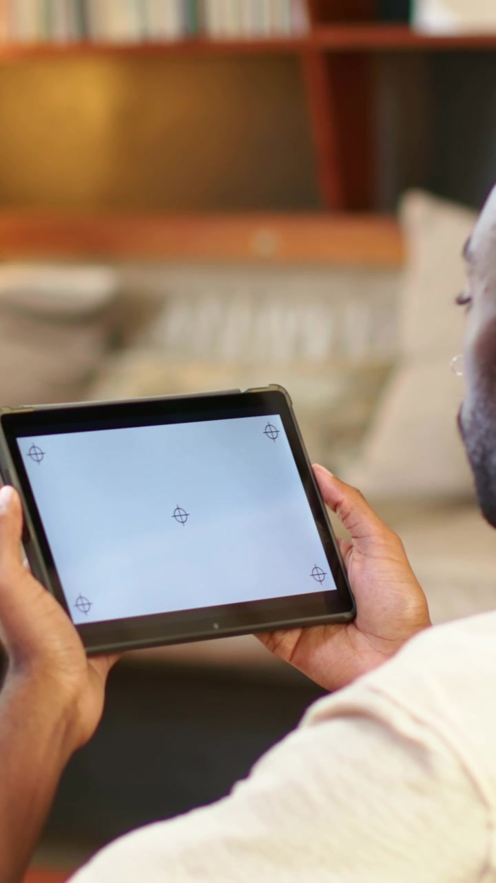 Vertical video: Moving tablet forward man in light tee adjusting grip on home sofa aligning markers