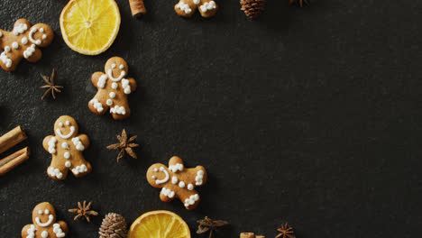 video of smiling gingerbread men and spices, slices of orange and nuts over black background