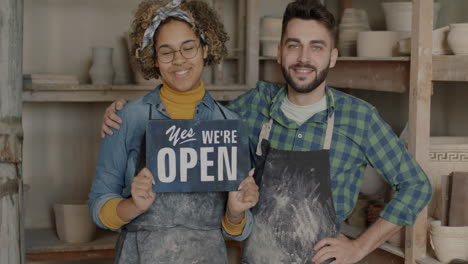 pottery studio owners smiling, showing 'open' sign