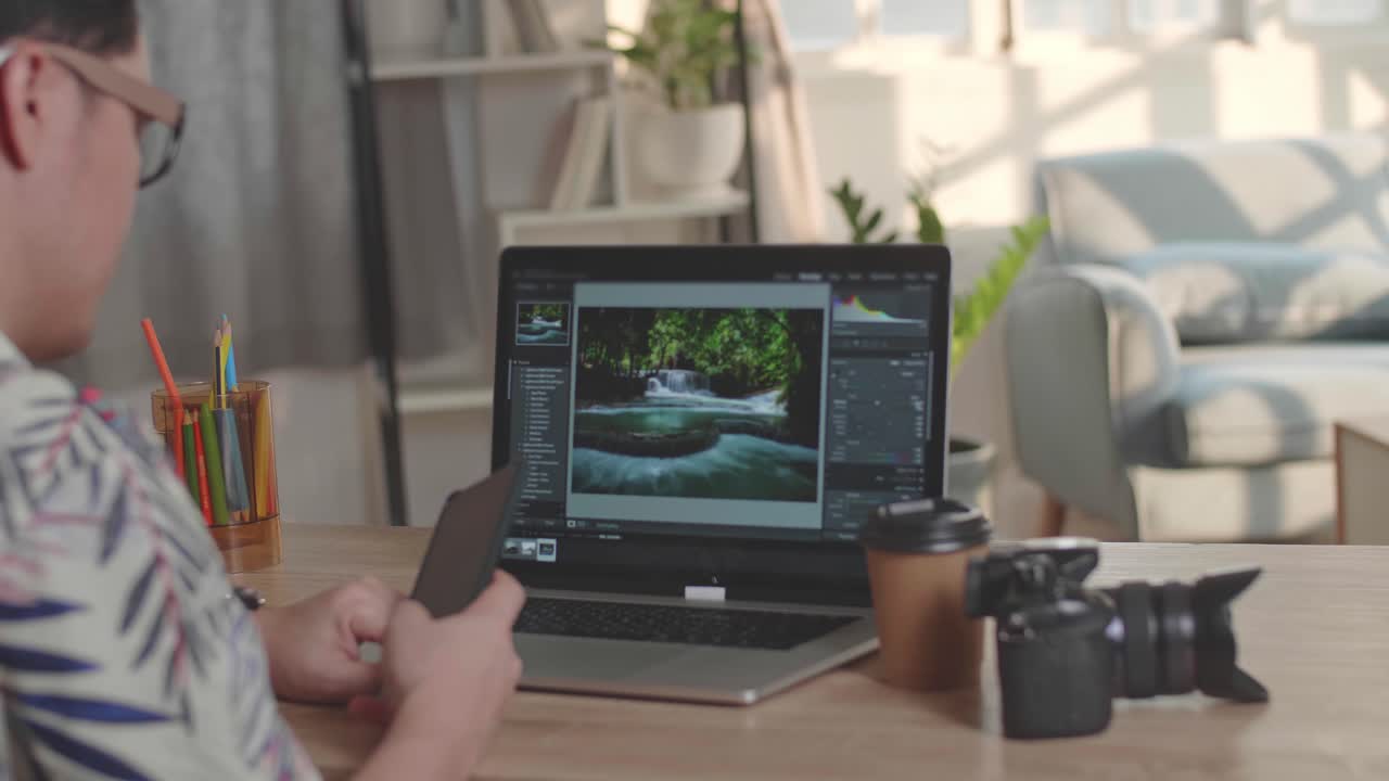 Photographer Talking On Mobile Phone With Photo Editing App / Software On His Laptop Computer