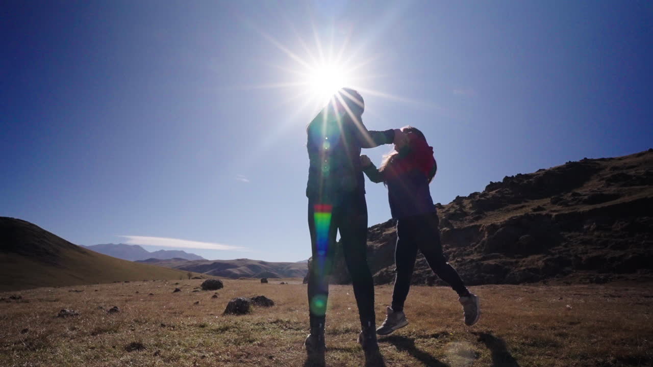 Silhouette of mother spinning her child under glowing sun in wide mountain valley
