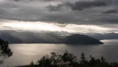 dense stormy clouds pierced by sun rays are carried by the strong wind above the dark hardanger fjord and mountains