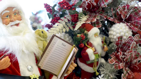 juguete de santa claus sosteniendo un bolígrafo y un cuaderno agradable y travieso con adornos navideños en el fondo