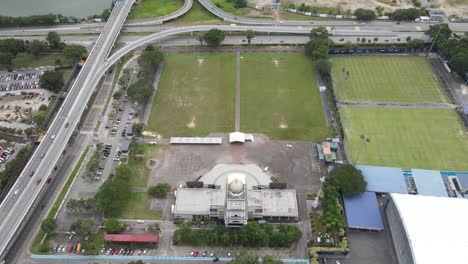 Una-Vista-De-Jam-Besar-Dataran-En-Johor-Bahru-Desde-Un-Dron-Aéreo-Con-Vistas-A-Los-Campos-De-Fútbol-Y-La-Autopista-En-Malasia