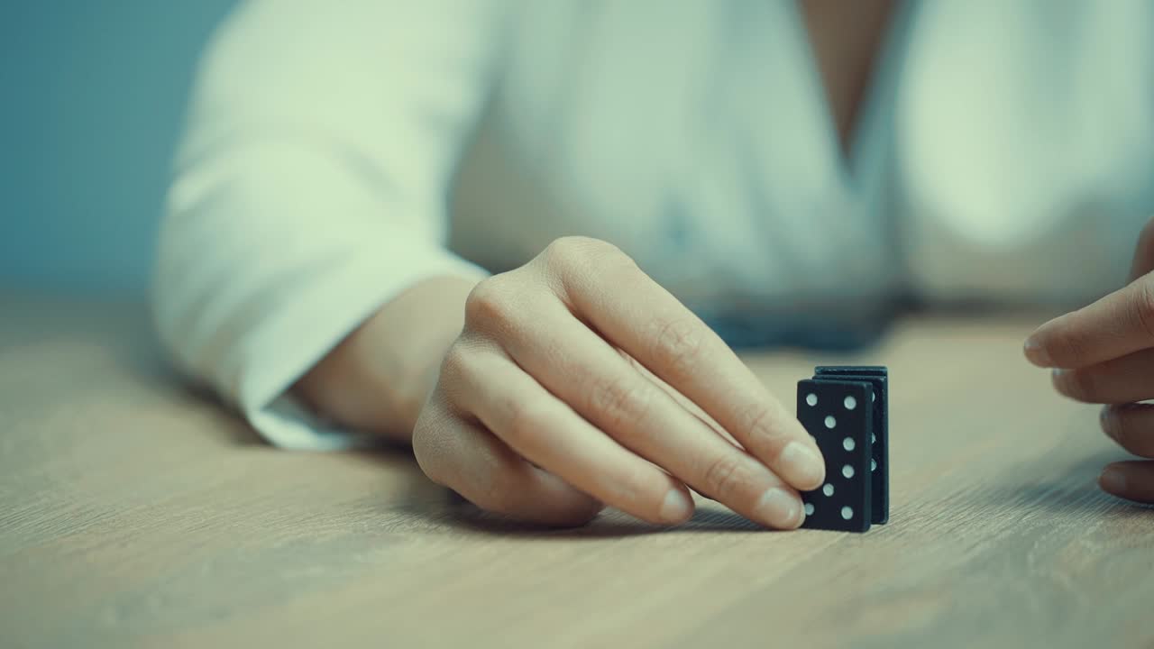 mano femenina de una mujer, vestida con un traje de negocios blanco destruyendo bloques de dominó, que están cayendo
