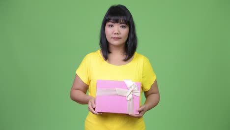 beautiful happy asian woman holding gift box while pointing up