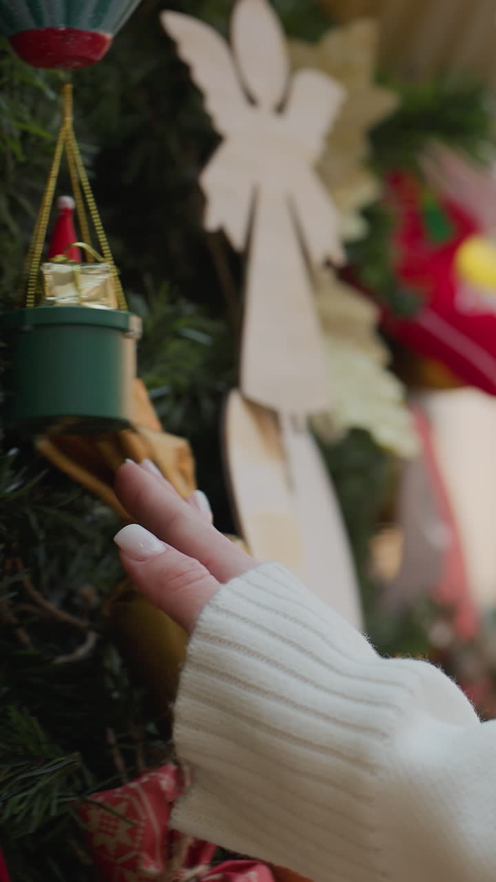 Close-up of lady in white sweater touching decorative Christmas tree affectionately in a shopping area, evoking a warm, festive atmosphere with soft holiday lights in the background