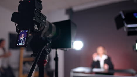 camera on tripod is filming a lady sitting at backdrop. close up. low angle view. video content creation in studio.