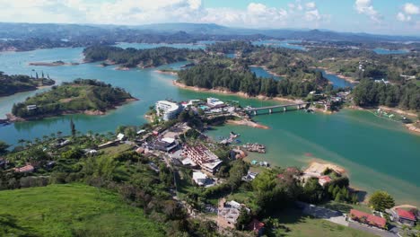 Vista-Aérea-Del-Lago-Guatape,-Colombia,-Edificios-Frente-Al-Lago-Y-Paisaje-Pintoresco-Bajo-El-Peñol,-Disparo-De-Drone