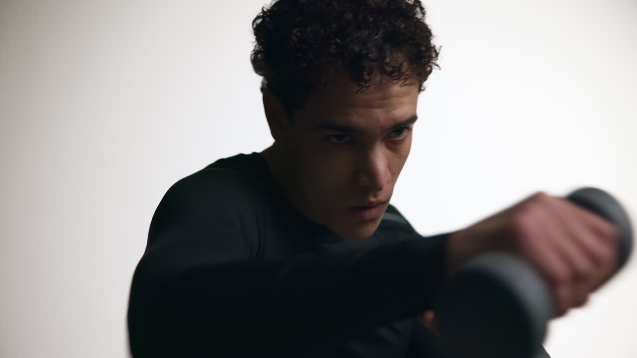 Determined Young Man Training with Dumbbells in a Studio