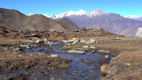 a small stream flowing down a hill with the himalyan mountains in the background in the mustang region of nepal