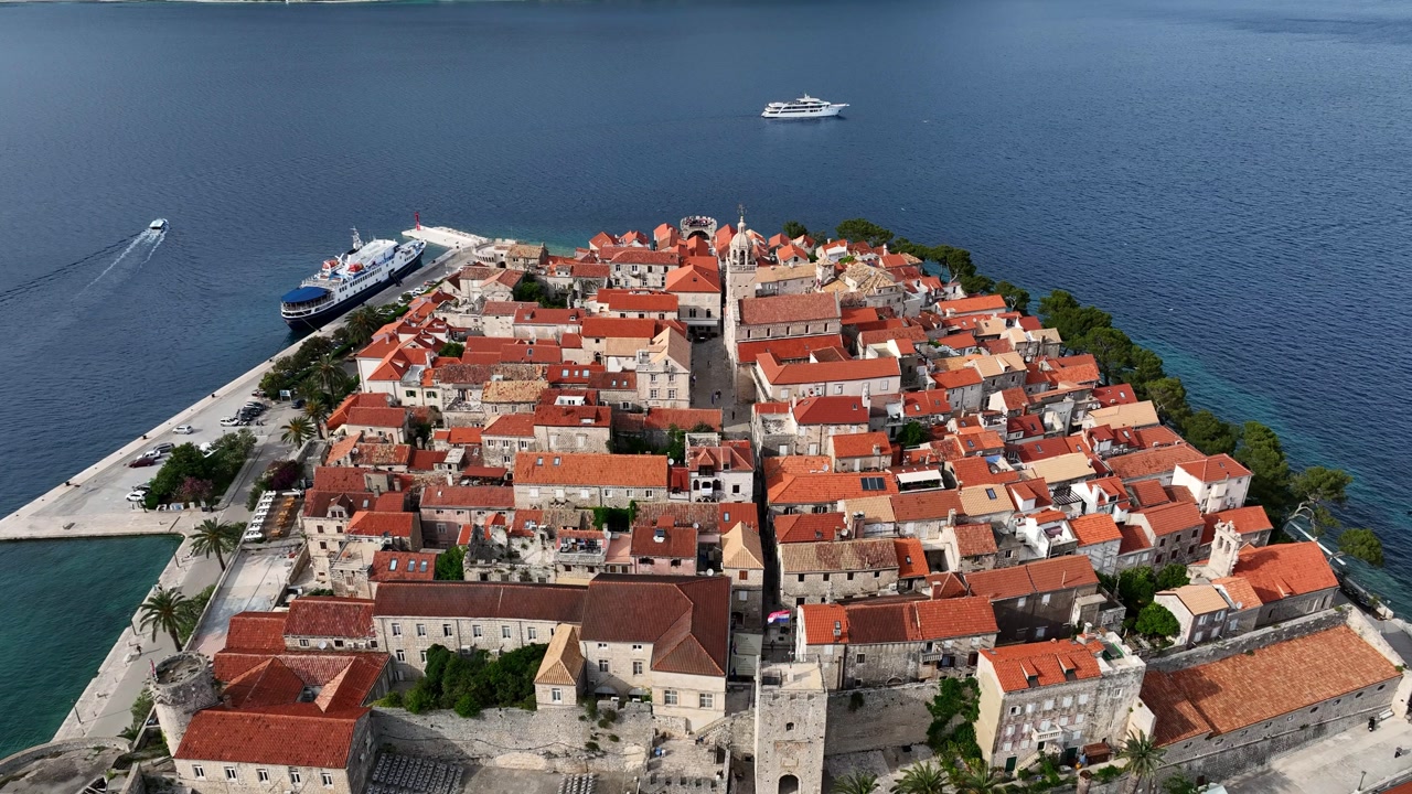 Historic Korcula Old Town with red tiled roofs on a small peninsula surrounded by Adriatic Sea, boats nearby. Aerial shot.