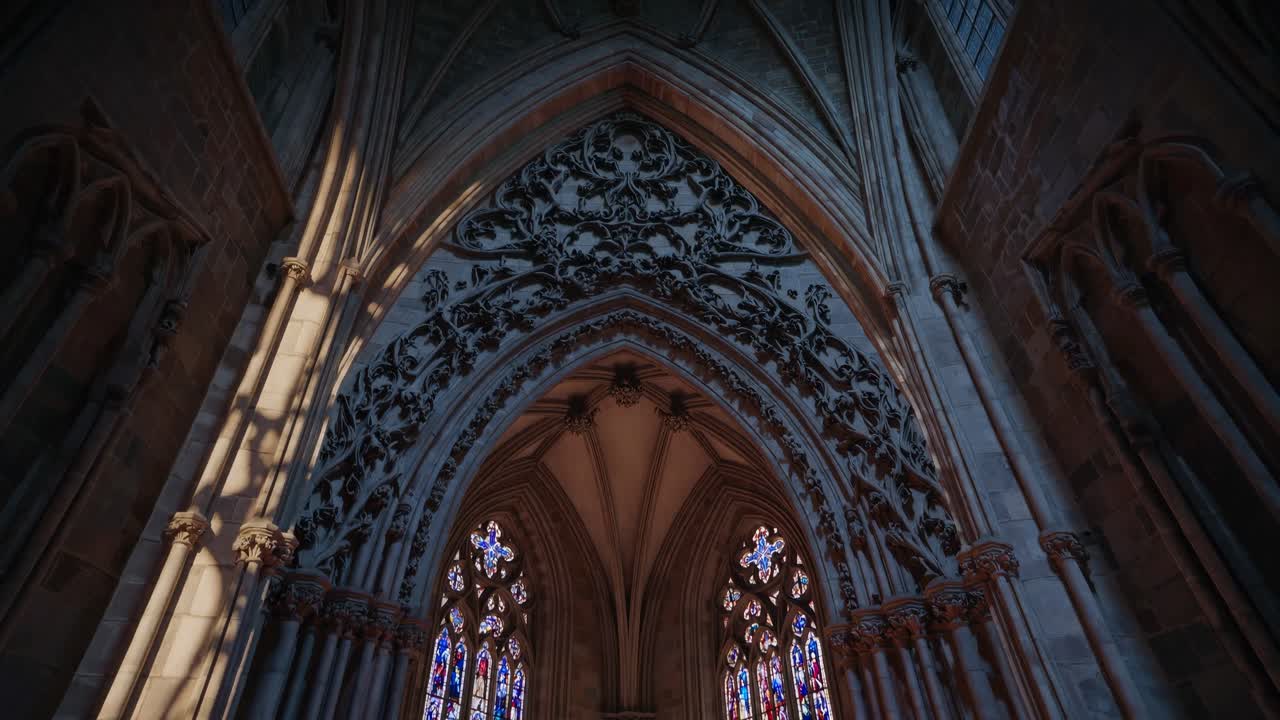 A low-angle video shot of a Gothic cathedral interior, highlighting intricate stained glass windows