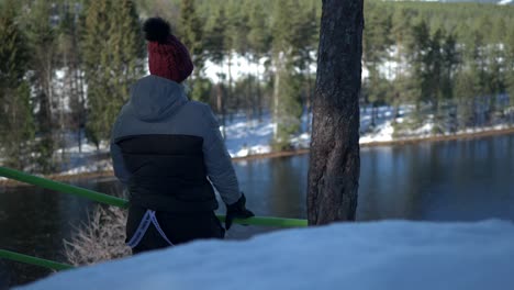 Nordic-Female-Looking-at-River-From-a-Hill,-Winter-Landscape-and-Boreal-Forest,-Static