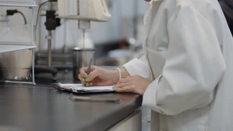 científica de bata blanca en el laboratorio tomando notas de investigación sobre experimentación