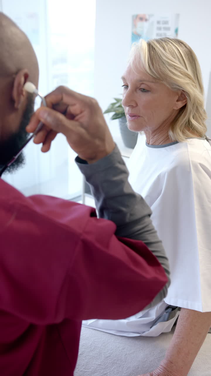 Vertical video of african american male doctor with stethoscope examining caucasian female patient