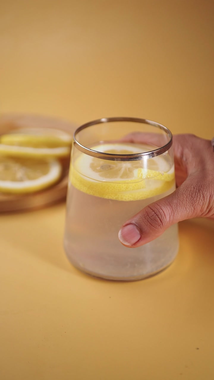 Hand Picking Up a Glass of Refreshing Lemon Water