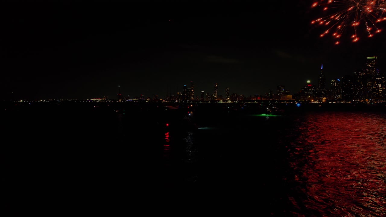 Esplosioni di fuochi d'artificio durante le feste sopra lo skyline urbano della città di Chicago e le acque scure e riflettenti