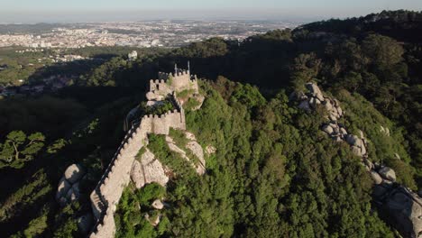 drone circling around medieval castle of the moors illuminated by sunlight standing at hilltop in the central portuguese above town of sintra, lisbon, portugal