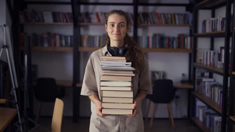 Smiling-student-holding-a-lot-of-books-in-the-library,-preparing-for-exams