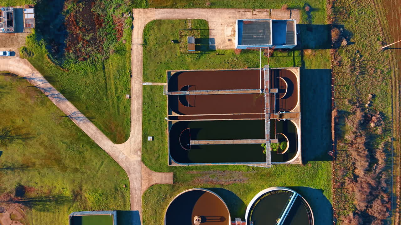 Water treatment facility in operation. Several water treatment tanks and facilities with green grass surrounding them during daylight hours