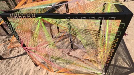 colorful string art within metal cubes on sandy beach