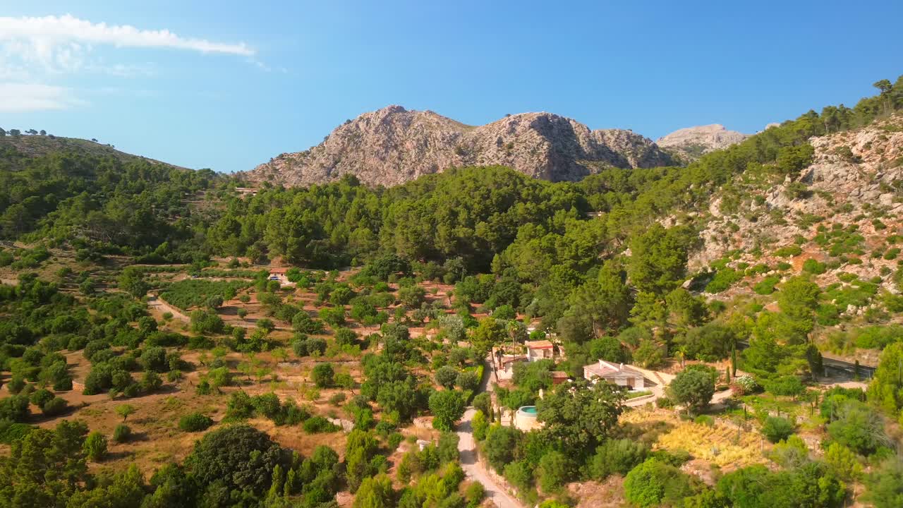 Lenta ripresa orbitale con drone attorno a una montagna rocciosa a Maiorca, in Spagna, con una lussureggiante foresta verde e una piccola finca visibile. Calda luce dell'ora d'oro sul paesaggio naturale, vista aerea ideale per viaggi e natura