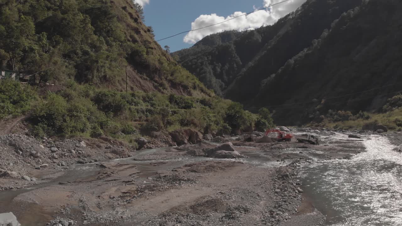 excavator digging rock out of river bed in mountainous region in Benguet Kabayan Philippines wide angle aerial approaching raw cement material mining
