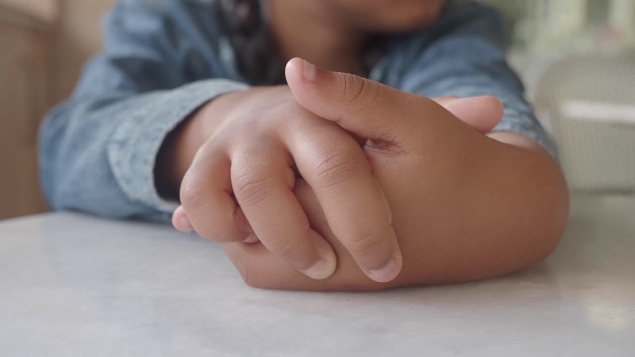 Close-up of a child's hands clasped on a table