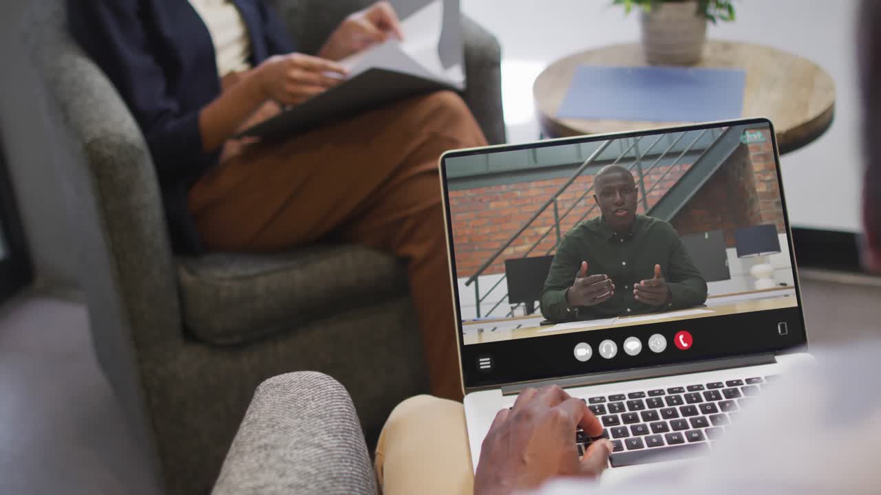 Uomo afroamericano che usa il laptop per una videochiamata, con un collega di lavoro sullo schermo
