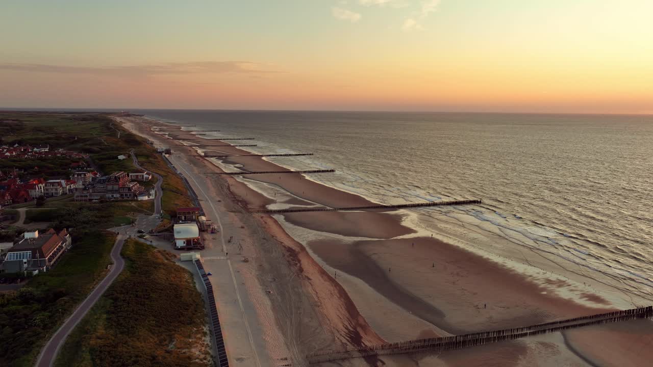 toma aérea de un pequeño pueblo costero a lo largo de una playa con espigones durante una hermosa puesta de sol sin nubes en verano