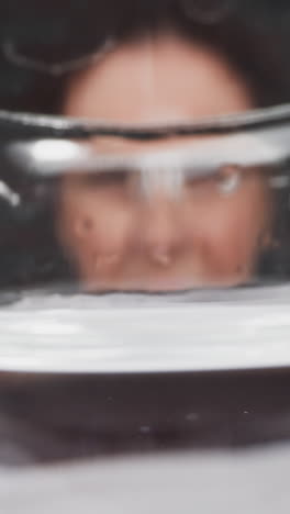 medical lady worker in gloves puts graduated beaker with transparent liquid in front of camera slow motion. probe lens footage of research work macro view
