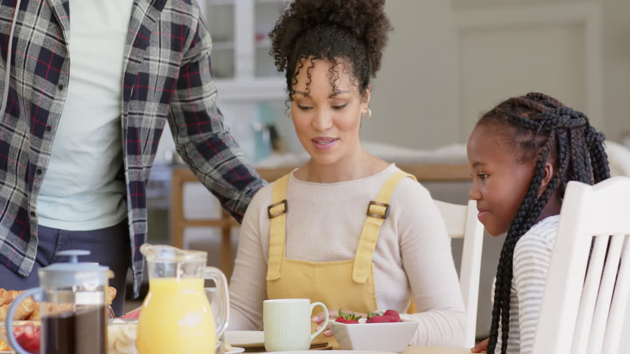 Glückliche afroamerikanische Eltern und Tochter frühstücken am Tisch, Zeitlupe