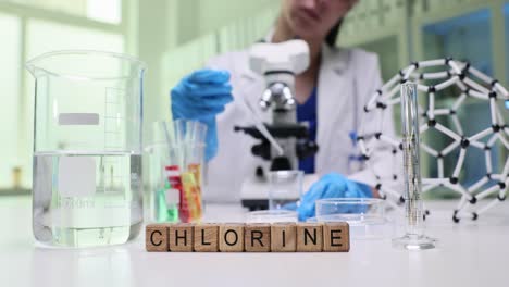 a person in a lab coat conducting a chemistry experiment in a laboratory, with the word 'chlorine' spelled out in wooden blocks