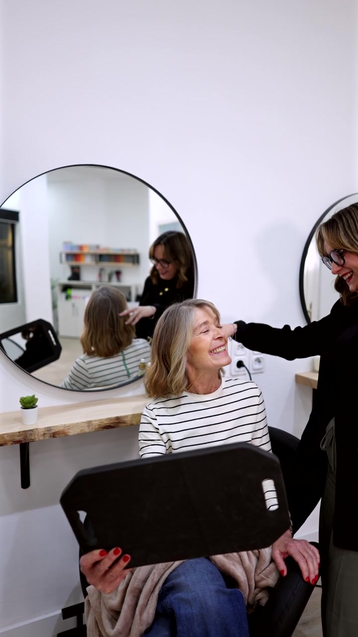 Donna anziana che si guarda la nuova acconciatura nello specchio di un salone.